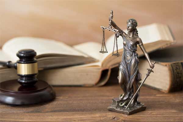 Libros legales, un mazo y la estatua de la justicia sobre un escritorio.
